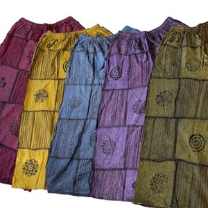 Könnte beinhalten: Fünf locker sitzende Hosen mit elastischem Bund und Kordelzug, die ein Patchwork-Design in Kastanienbraun, Gelb, Blau, Lila und Olivgrün aufweisen. Jede Hose ist mit schwarzen kreisförmigen Sonnen- und Blumenmotiven verziert.