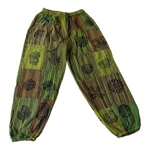 Könnte beinhalten: Weit geschnittene Hose mit einem Patchwork-Design aus grün und braun gestreiften Stoffbahnen. Die Hose ist mit schwarzen, blockgedruckten Blumen- und Pflanzenmotiven, einem elastischen Bund mit Kordelzug und elastischen Beinabschlüssen versehen.