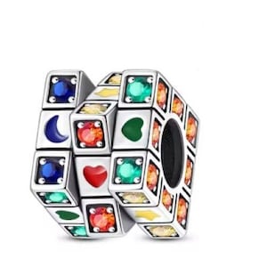 May include: A silver charm with a geometric design, featuring various colored gemstones and symbols. The charm includes blue, green, red, and yellow stones, along with heart, crescent moon, and arrow symbols. The charm has a hole for a bracelet or necklace.