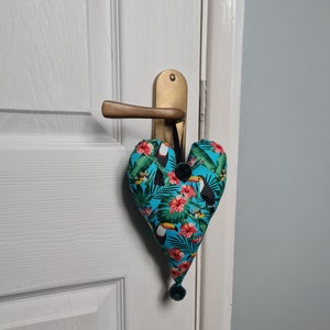 May include: A blue heart-shaped doorstop with a tropical print featuring toucans and flowers. The doorstop is hanging from a door handle.