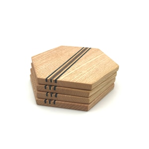 Può includere: Set di quattro sottobicchieri esagonali in legno con strisce di intarsio nere e marroni. I sottobicchieri sono impilati uno sopra l'altro.