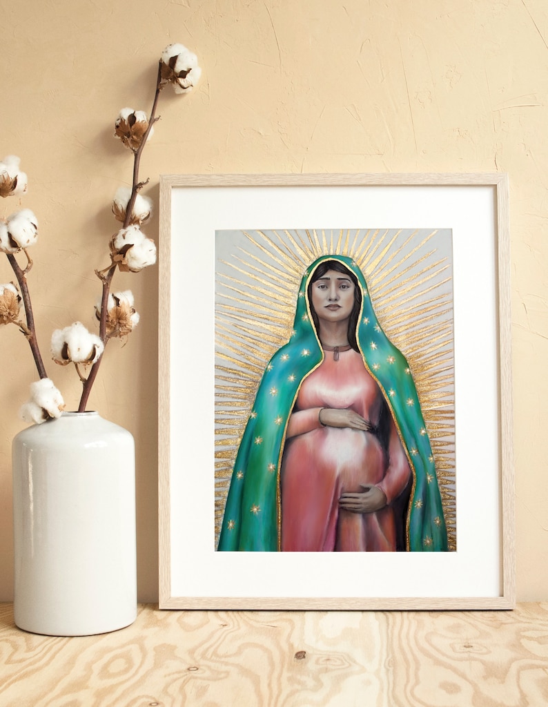 May include: A framed print of a painting depicting a woman in a blue and green robe with a gold halo. She is pregnant and holding her belly. The background is a light gray with gold accents.