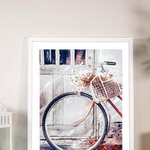 May include: A white bicycle with a wicker basket filled with white flowers is parked in front of a weathered wooden door. The bicycle wheel is in focus, and the door is out of focus.