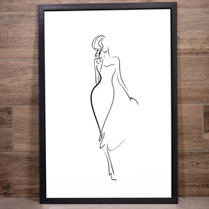 May include: A framed black and white line art print. The artwork depicts a woman in a flowing dress, rendered with simple, elegant lines. The minimalist design is set against a white background, framed in a black border.