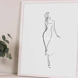 May include: A framed minimalist art print featuring a black line drawing of a woman in a flowing dress. The artwork is set against a white background within a white frame. The text "DECORIDIC" is visible on the artwork.