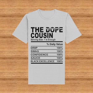 May include: A gray t-shirt with a black graphic that reads "Unapologetically The Dope Cousin" with a nutrition label underneath that says "Serving Size: 1 Is Enough" and lists "Drip, Swag, Confidence, Sauce, Black Excellence" with a value of 100% for each.