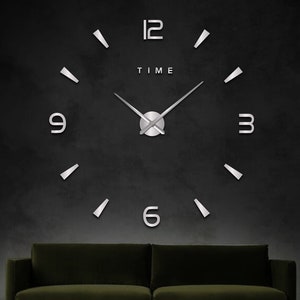 May include: A large, silver, 3D wall clock with black hands and the word "TIME" printed on the face. The clock is mounted on a dark grey wall above a dark green sofa.