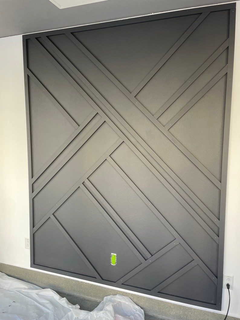 Op de afbeelding: Een donkergrijze muur met een geometrisch patroon gecre&euml;erd door houten stroken. De stroken zijn in een kruispatroon gerangschikt, wat een moderne en stijlvolle uitstraling cre&euml;ert.