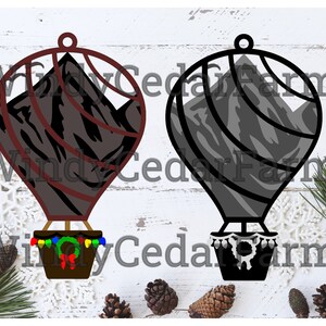 Peut inclure: Deux décorations de montgolfières noires et grises avec des motifs de montagnes. La montgolfière de gauche a un contour rouge et une couronne de Noël avec des lumières autour du panier. La montgolfière de droite a un contour noir et une bordure blanche autour du panier.