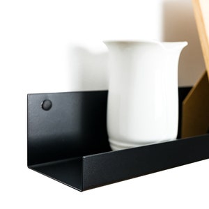 Modern floating metal picture ledge made of 1.5 mm cold-rolled steel, with rounded corners and front lip. Ideal for framed photos, art prints, books, spices or decor. Powder-coated in black, black matt, white, white matt, or brushed stainless steel for industrial, minimalist, or Scandinavian interiors. Wall-mounted with hidden hardware. Available in custom RAL colors and lengths up to 240 cm.