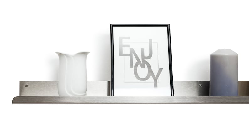 May include: A stainless steel shelf with a white vase, a framed print with the word "ENJOY" in silver lettering, and a gray candle.
