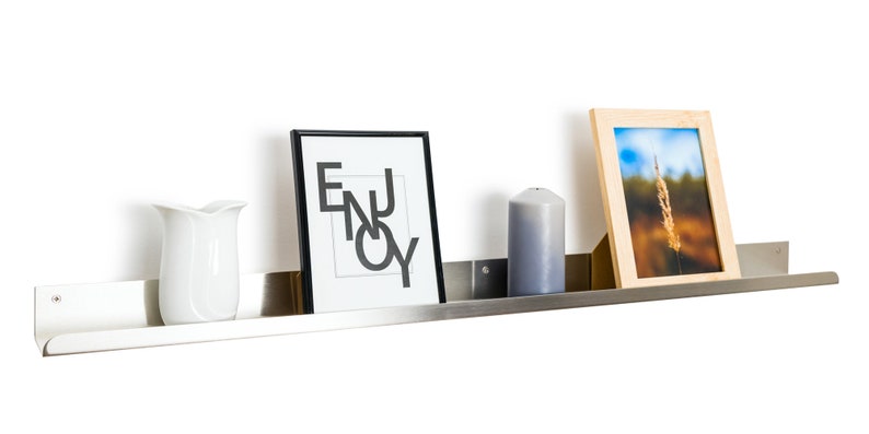 May include: A silver metal shelf with a white ceramic pitcher, a framed print with the word "ENJOY" in black lettering, a gray candle, and a framed photograph of a tall grass stalk against a blue sky.