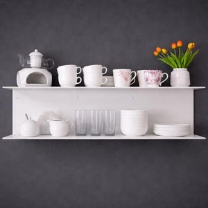 K&ouml;nnte beinhalten: Wei&szlig;e Regale vor einer dunkelgrauen Wand zeigen verschiedene K&uuml;chenartikel. Das obere Regal enth&auml;lt Tassen, einen Teew&auml;rmer und eine Vase mit orangefarbenen Tulpen. Das untere Regal zeigt Gl&auml;ser, einen Sahnek&auml;nnchen und Schalen.