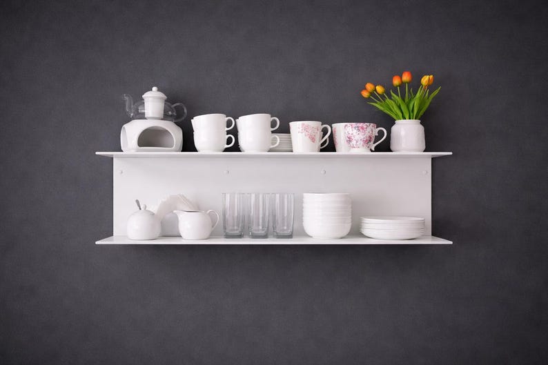 K&ouml;nnte beinhalten: Wei&szlig;e Regale vor einer dunkelgrauen Wand zeigen verschiedene K&uuml;chenartikel. Das obere Regal enth&auml;lt Tassen, einen Teew&auml;rmer und eine Vase mit orangefarbenen Tulpen. Das untere Regal zeigt Gl&auml;ser, einen Sahnek&auml;nnchen und Schalen.