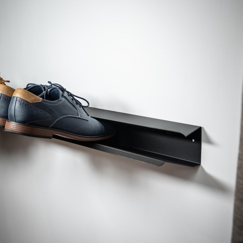 Peut inclure: Un porte-chaussures en m&eacute;tal noir mont&eacute; sur un mur blanc avec une paire de chaussures en cuir bleu sur le porte-chaussures.
