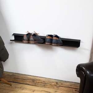 Peut inclure: Un porte-chaussures en m&eacute;tal noir mont&eacute; sur un mur blanc avec deux paires de chaussures.