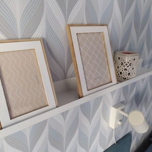 May include: Two white picture frames with wooden trim, one with a geometric pattern and the other with a chevron pattern, are displayed on a white shelf against a blue and white patterned wallpaper. The frames are labeled with their dimensions: 13x18cm and 11x16cm.