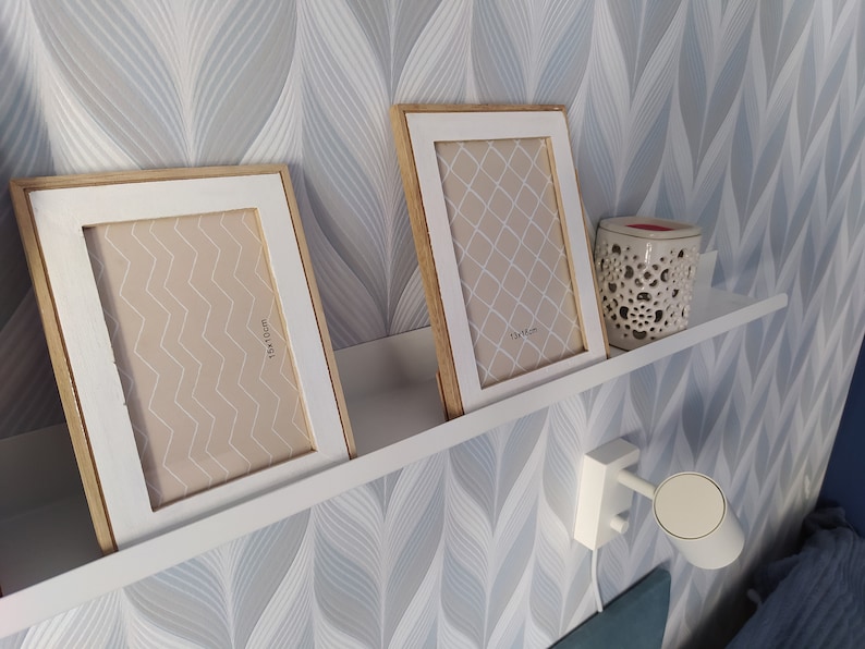 May include: Two white picture frames with wooden trim, one with a geometric pattern and the other with a chevron pattern, are displayed on a white shelf against a blue and white patterned wallpaper. The frames are labeled with their dimensions: 13x18cm and 11x16cm.