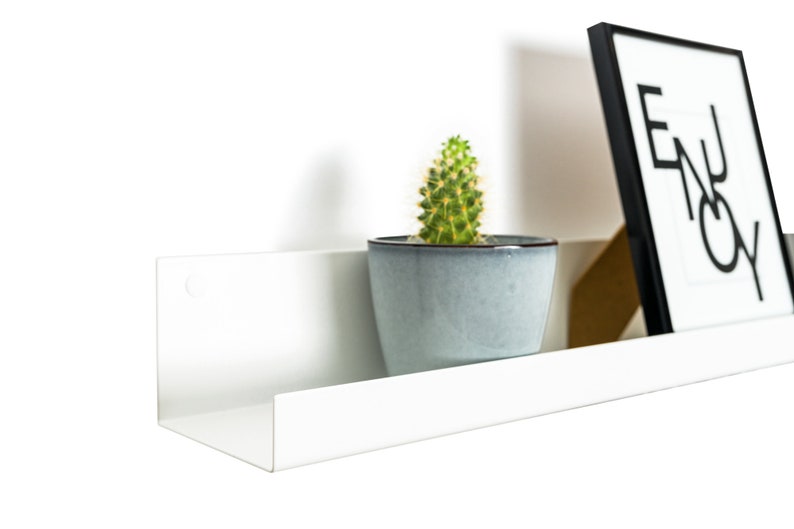 Modern floating metal picture ledge made of 1.5 mm cold-rolled steel, with rounded corners and front lip. Ideal for framed photos, art prints, books, spices or decor. Powder-coated in black, black matt, white, white matt, or brushed stainless steel for industrial, minimalist, or Scandinavian interiors. Wall-mounted with hidden hardware. Available in custom RAL colors and lengths up to 240 cm.