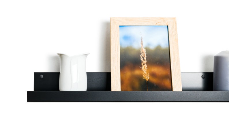 Modern floating metal picture ledge made of 1.5 mm cold-rolled steel, with rounded corners and front lip. Ideal for framed photos, art prints, books, spices or decor. Powder-coated in black, black matt, white, white matt, or brushed stainless steel for industrial, minimalist, or Scandinavian interiors. Wall-mounted with hidden hardware. Available in custom RAL colors and lengths up to 240 cm.