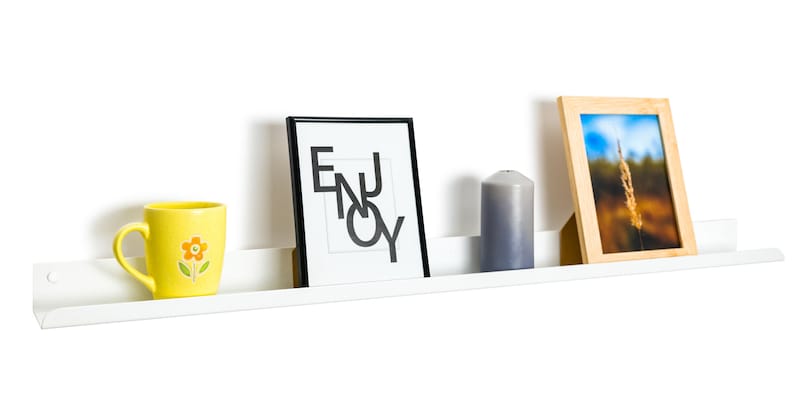May include: White floating shelf with a yellow mug with a flower design, a black framed print with the word "ENJOY" in white, a gray candle, and a wooden framed photo with a landscape scene.