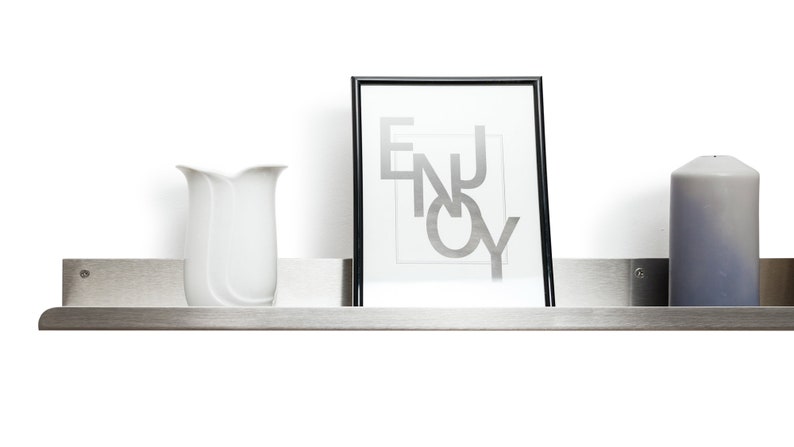 May include: A stainless steel shelf with a white vase, a framed print with the word "ENJOY" in silver lettering, and a gray candle.