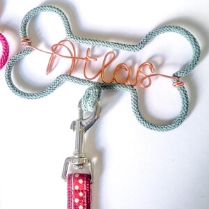 close up of A grey marl dog leash hook,  with a the name Atlas in copper wire.