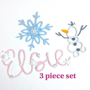 May include: A pink and white 3 piece set of Frozen themed cake toppers. The set includes a snowflake, a snowman, and the name "Elsa" spelled out in pink.
