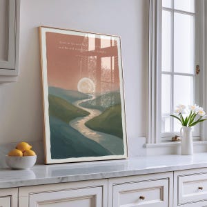 May include: Framed art print featuring a landscape scene with a river winding through green hills under a large moon. The artwork has a warm color palette with text at the top. The frame is gold.