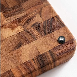 May include: A brown wooden cutting board with a checkered pattern. The board has a black rubber foot on the bottom.