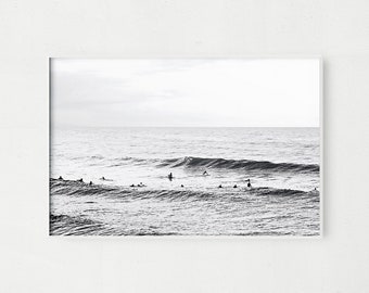 May include: Black and white photograph of a group of surfers in the ocean. The surfers are silhouetted against the waves and the sky. The photo has a minimalist aesthetic.