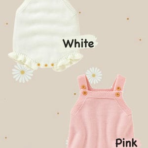 May include: Two knitted baby rompers, one white and one pink, with wooden button details. The white romper has the word "White" and the pink romper has the word "Pink" written on it. Both rompers have a ruffled hem.