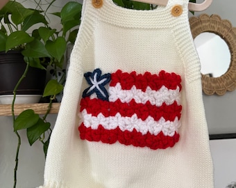 May include: White knitted baby romper with a red, white, and blue crocheted American flag design on the front.