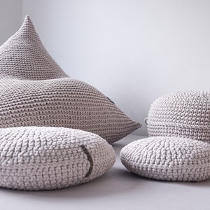 May include: A set of four beige knitted poufs, including a large, triangular pouf and three smaller round poufs. The poufs are made of a soft, textured fabric and are perfect for adding a touch of comfort and style to any room.