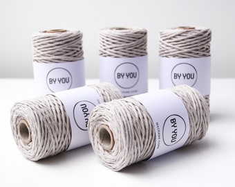 Könnte beinhalten: Fünf Spulen hellgrauer Makrameeschnur mit dem Etikett "BY YOU MACRAME CORD" auf jeder Spule.
