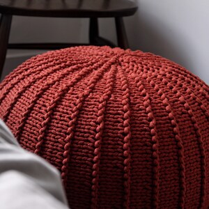 May include: A large, round, red knitted ottoman with a textured surface.