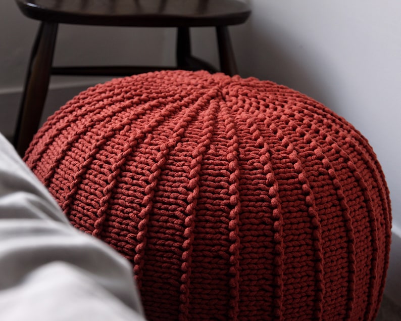 May include: A large, round, red knitted ottoman with a textured surface.