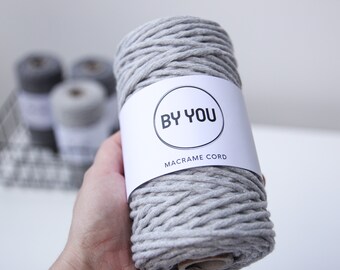 Könnte beinhalten: Eine Rolle graue Makramee-Schnur mit einem weißen Etikett, auf dem "BY YOU MACRAME CORD" steht.