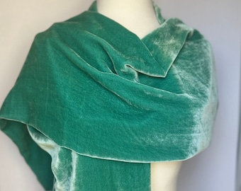 May include: A soft, green velvet scarf draped over a mannequin. The scarf is made of a luxurious fabric and has a subtle sheen.