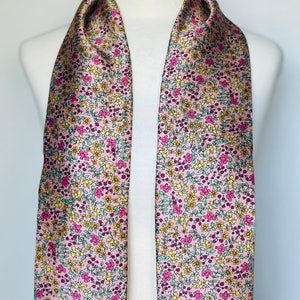 May include: A pink satin scarf with a floral pattern in shades of yellow, green, and pink.