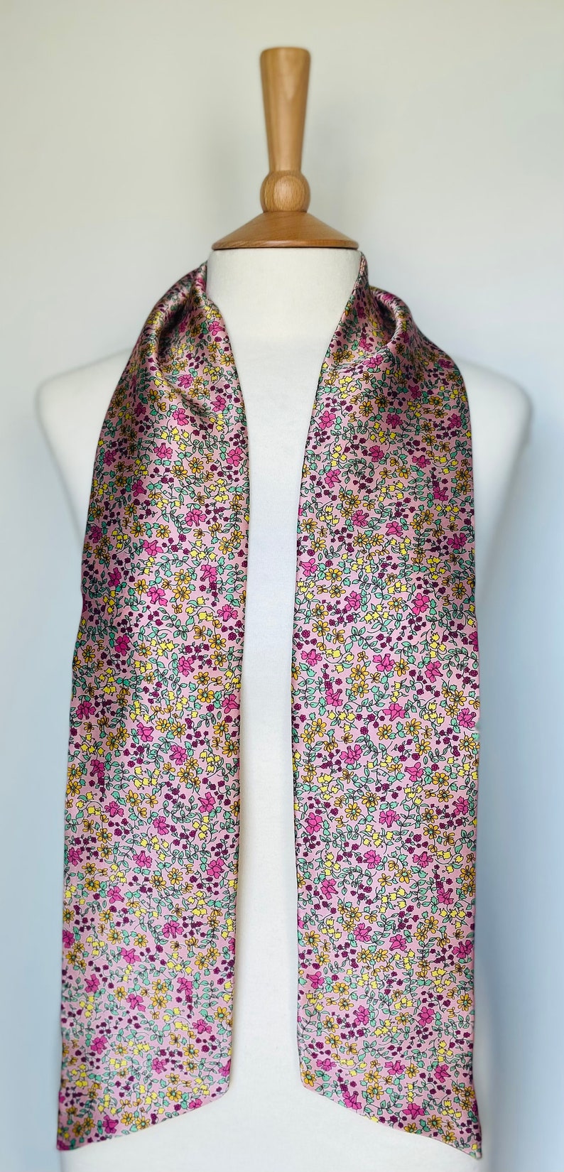 May include: A pink satin scarf with a floral pattern in shades of yellow, green, and pink.