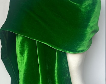 May include: A vibrant green velvet shawl draped over a mannequin. The fabric has a rich, lustrous sheen, and the folds create shadows that highlight the texture. The shawl is a solid color, and the mannequin is white.