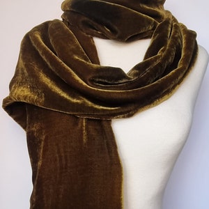 May include: A long, olive green velvet scarf draped over a white mannequin. The scarf is soft and luxurious, with a subtle sheen.