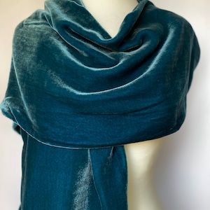 May include: A teal blue velvet scarf draped over a mannequin. The scarf is soft and luxurious, with a subtle sheen.