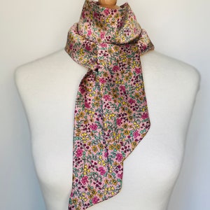 May include: A pink silk scarf with a floral pattern in shades of yellow, green, and pink.
