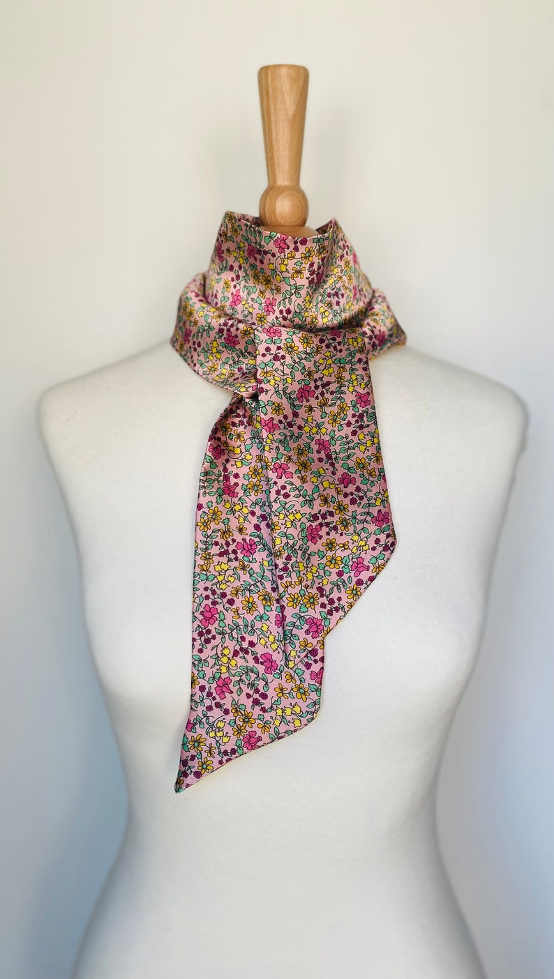 May include: A pink silk scarf with a floral pattern in shades of yellow, green, and pink.