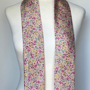 May include: A long, pink scarf with a floral pattern. The scarf has small pink, yellow, and green flowers on a light pink background.