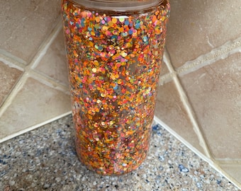 May include: A clear glass tumbler with a bamboo lid filled with colorful confetti. The tumbler is sitting on a speckled countertop.