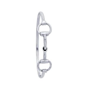 May include: A silver-colored bangle bracelet featuring a horse bit design. The bracelet has a simple, elegant style with a curved band and a detailed bit charm. The bit charm has two rounded rings connected by a central bar.