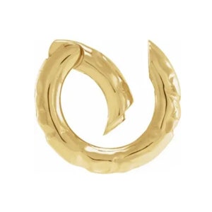 May include: A gold-colored earring with a textured, hammered finish. The earring has a curved, open design, with a portion that appears to overlap. The overall shape is circular, with a slightly irregular form. The earring is set against a white background.